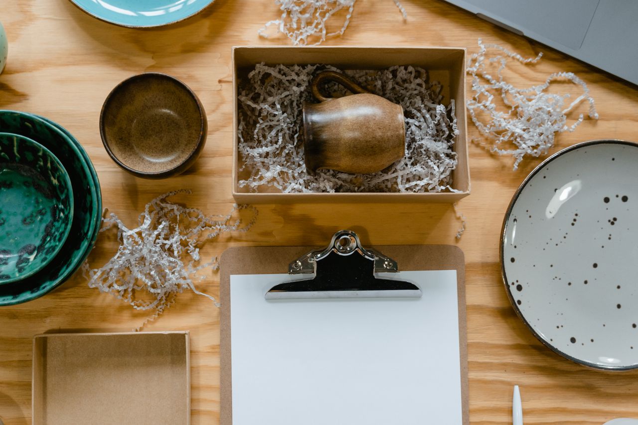 footer-cta-img Flat lay of ceramic bowls and a mug in eco-friendly packaging with clipboard on a wooden table.